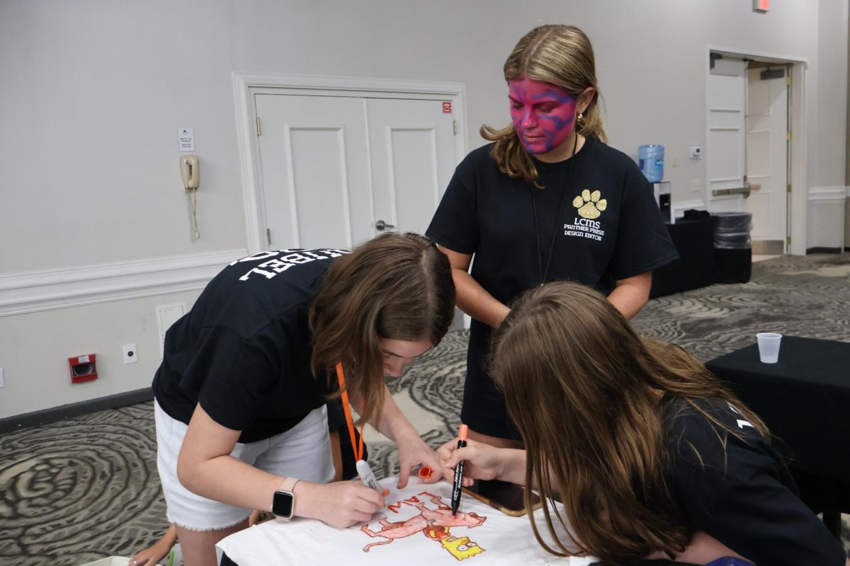Students Emily, Audrey, and Harper work on Annabelle’s shirt for the contest.