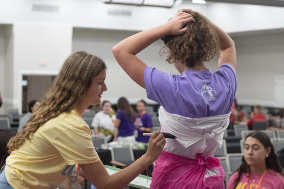 Angeline Academy students cooperate with each other as one leans over to draw on the cut and tied T-shirt as junior Tessa Sevelius prepares for her fashion show debut. 