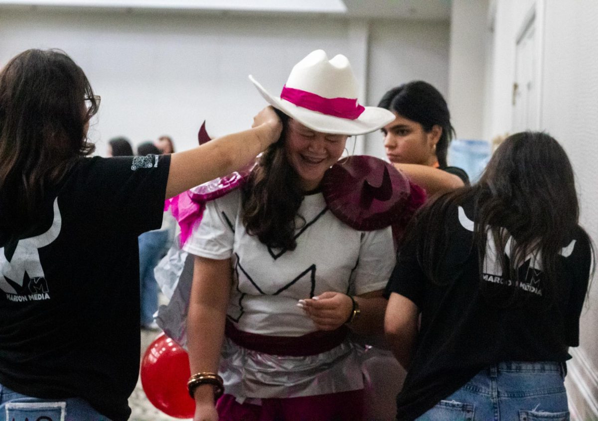 Wiregrass Ranch High School students pin maroon balloons and shiny decorations to their friend’s back, securing the bits and pieces of the costume before the show.