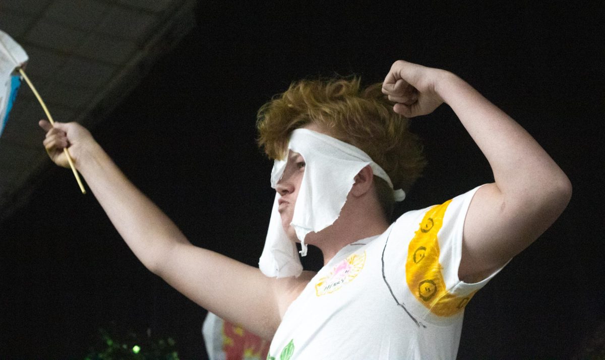A student raises his school's spirit flag high with his right arm and flexes his left arm at the end of the fashion show.